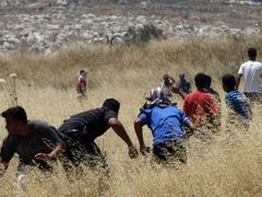 Mladí Palestinci házejí kameny na skupinku židovských osadníků u Nábulusu na západním břehu Jordánu.
