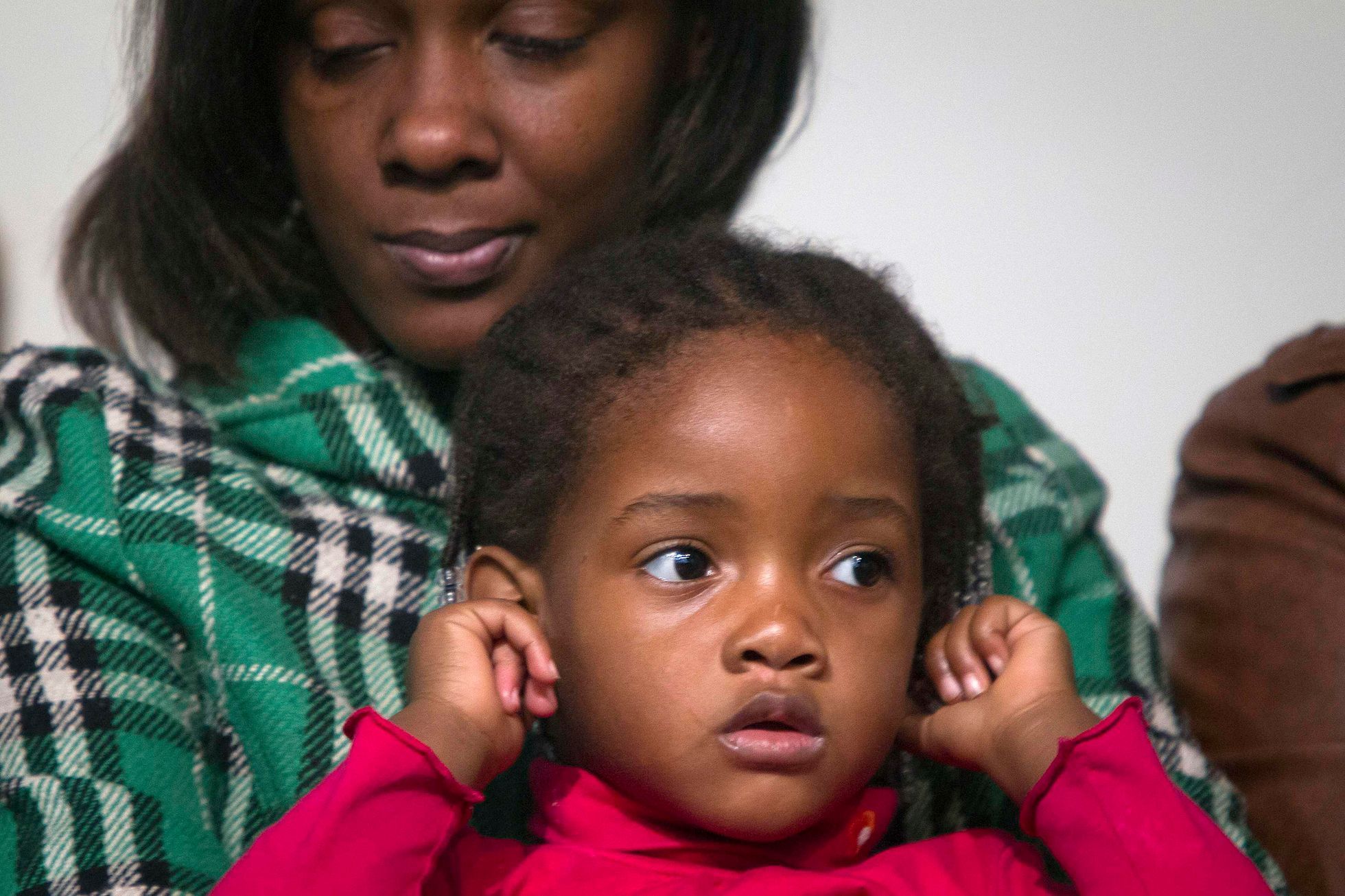 Akai Gurley's daughter Akaila sits on her mother Kimberly Ballinger's lap and plugs her ears as civil rights activist Reverend Al Sharpton speaks in the Harlem Borough of New York