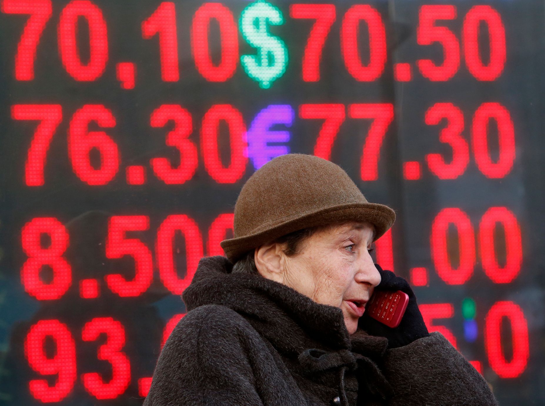 Žena mluví do telefonu před tabulí se směnnými kurzy rublu.