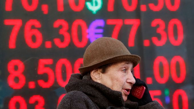 Žena mluví do telefonu před tabulí se směnnými kursy rublu.