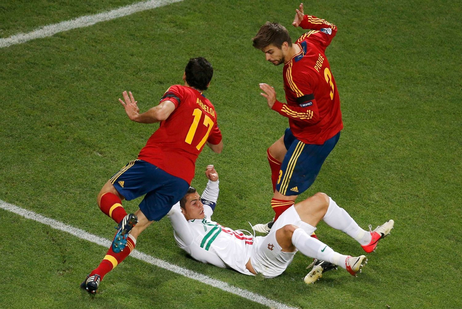 Španělští fotbalisté Alvaro Arbeloa a Gerard Piqué se vyhýbají ležícímu Portugalci Cristianu Ronaldovi během semifinále na Euru 2012.