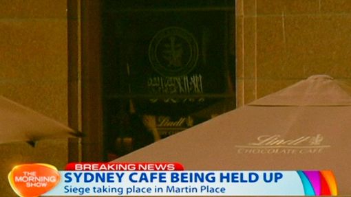 V okně kavárny Lindt Chocolat Cafe v australském Sydney, kde drží ozbrojený útočník rukojmí, byla vyvěšena černobílá vlajka s arabským nápisem.