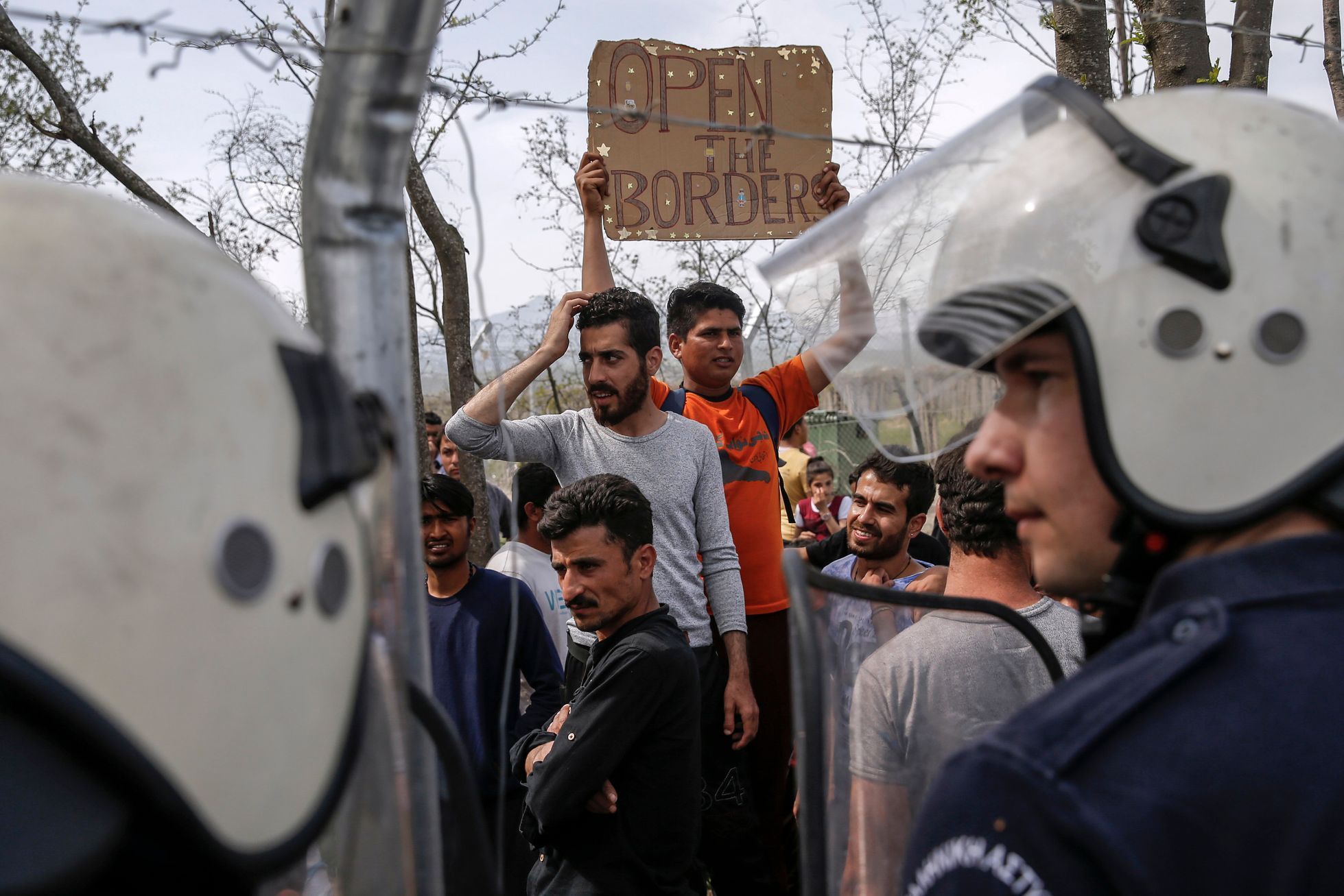 Migrants and refugees stand in front of Greek policeman after they tried to open the border fence at a makeshift camp at the Greek-Macedonian border near the village of Idomeni