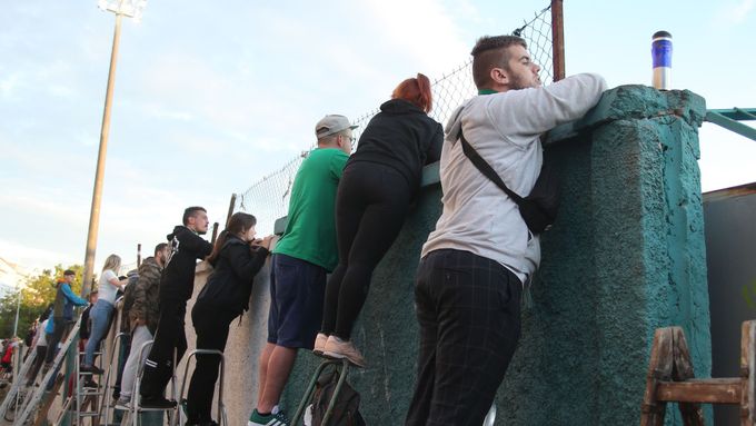 Fanoušci Bohemians přihlíží zpoza zdi stadionu zápasu proti Spartě.
