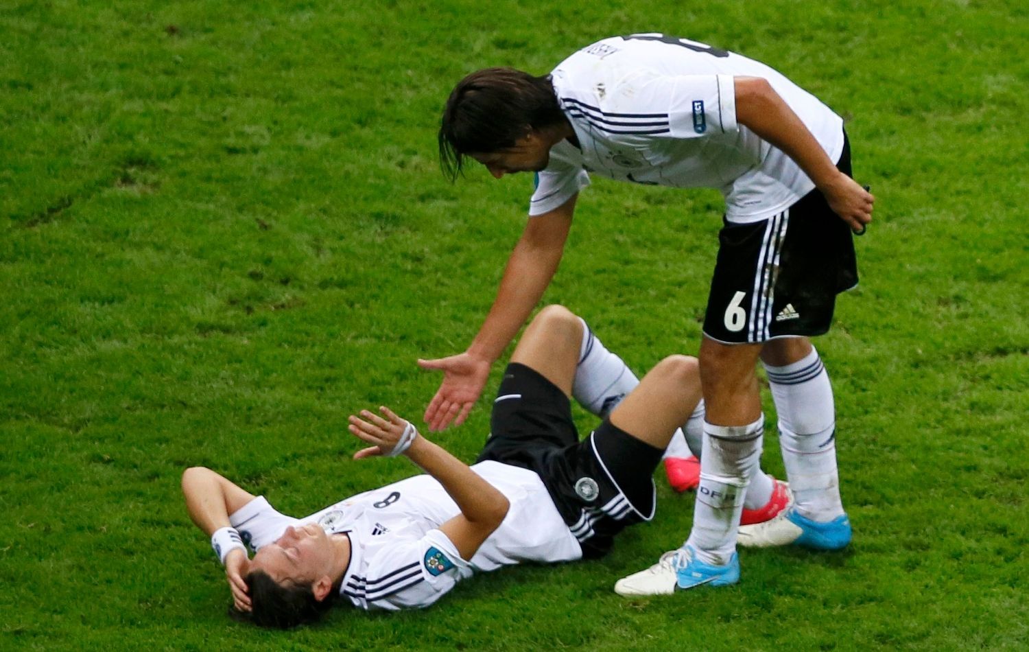 Sami Khedira pomáhá ze země Mesutu Özilovi v semifinálovém utkání Eura 2012 mezi Německem a Itálií.