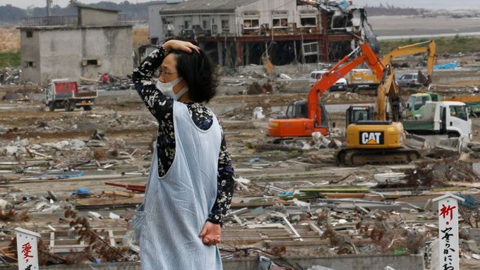 Žena sleduje odklízení trosek v poničeném městě Natori. Snímek z června 2011. Ilustrační foto.