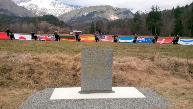 Pomník na místě leteckého neštěstí. V pozadí vlajky států, z nichž pocházely oběti.