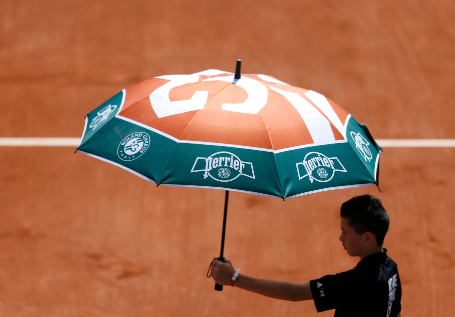 A court boy holds an umbrella during the women's singles match betwween Simona Halep of Romania and Evgeniya Rodina of Russia at the French Open tennis tournament at the Roland Garros stadium in Paris