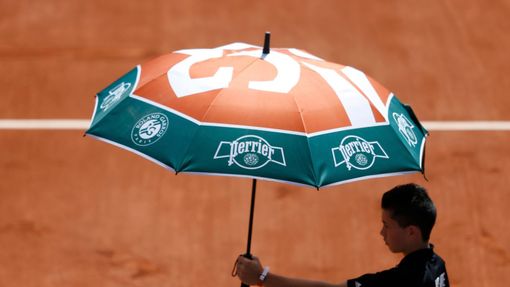 A court boy holds an umbrella during the women's singles match betwween Simona Halep of Romania and Evgeniya Rodina of Russia at the French Open tennis tournament at the