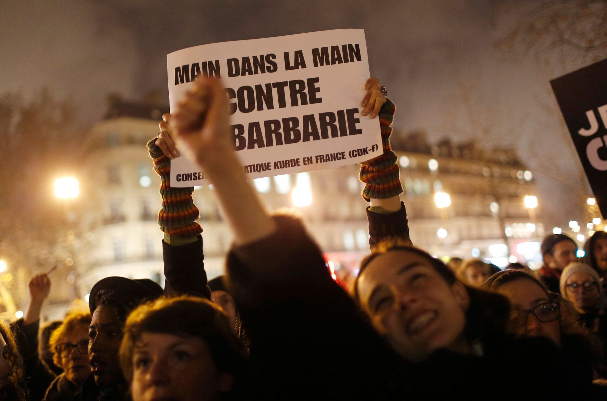 A woman holds a placard that reads, &quot;Hand in hand against barbarity&quot;, during a vigil to pay tribute to the victims of a shooting by gunmen at the offices of weekly satirical magazine Charlie