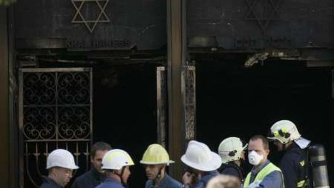 Hasiči stojí před ohořelou synagogou.