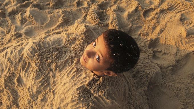 Palestinský chlapec se nechal na pláži zahrabat do písku a užívá si teplého počasí na městské pláži v Gaze.