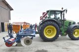 Stroj zapřažený za traktor vytváří v půdě rýhu, do které klade otrávenou návnadu.