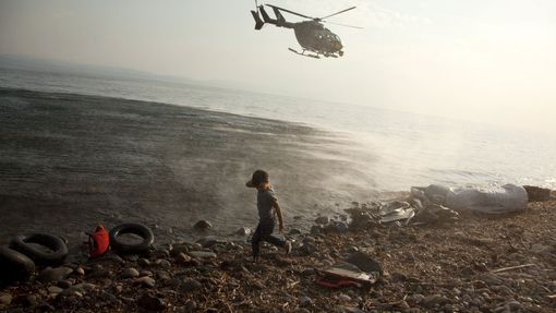 Vrtulník evropské agentury Frontex přelétá u syrského chlapce, který se právě vylodil na řeckém ostrově Lesbos. Tam běženci momentálně tvoří zhruba pětinu lidí.