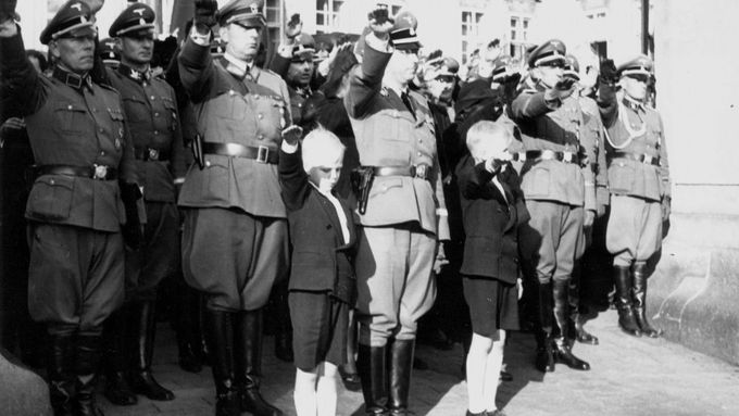Nacisté hajlující s ostatními lidmi v protektorátu památce Reinharda Heydricha. V popředí protektorovy děti.
