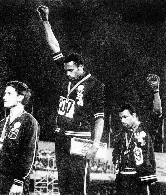 Američtí atleti Tommie Smith a John Carlos zdvihli ruku v černé rukavici zaťatou v pěst, aby ukázali podporu boje proti rasismu.