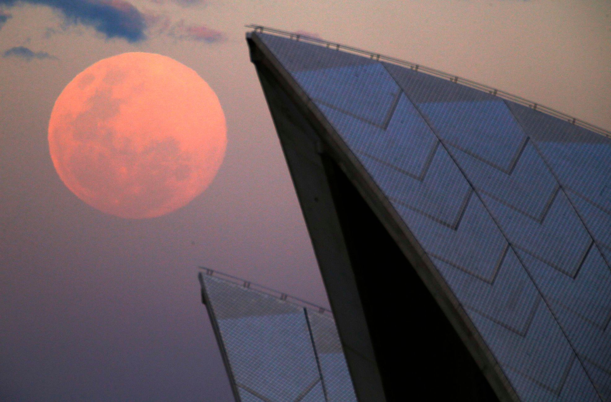A supermoon rises behind the roof of the Sydney Opera House