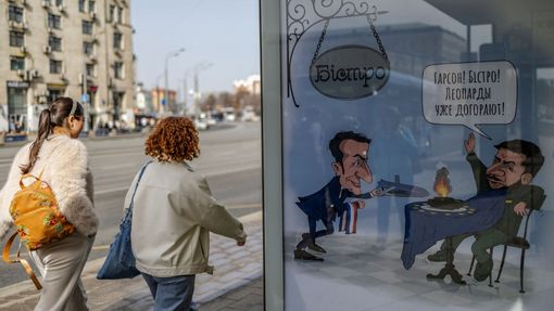 Kreslený vtip na moskevské autobusové zastávce. Ukajinský prezident Volodymyr Zelenskyj "komanduje" ve francouzském bistru číšníka Emmanuela Macrona.
