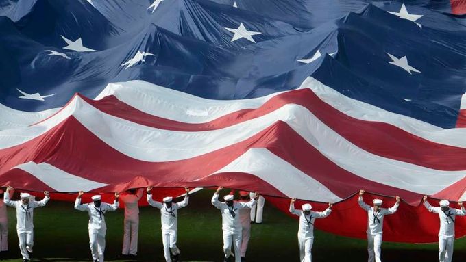 America First! Hvězdy a pruhy mají napříště vlát především doma. (Američtí námořníci rozbalují vlajku Spojených států u příležitosti zahájení Major League Baseball.)