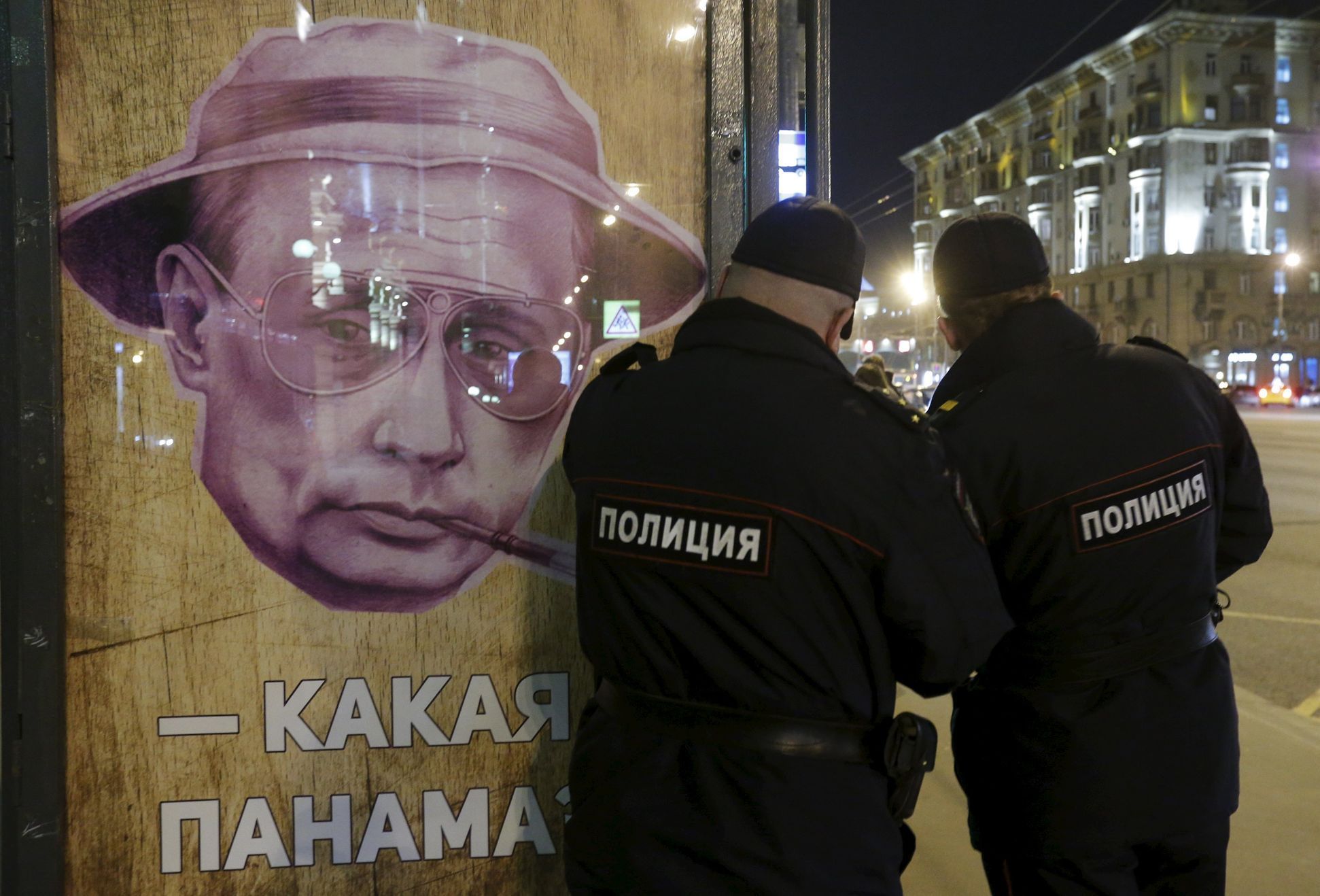 Policisté u plakátu s Putinem na autobusové zastávce v Moskvě.