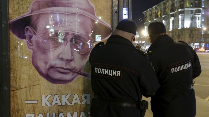 Policisté u plakátu s Putinem na autobusové zastávce v Moskvě.