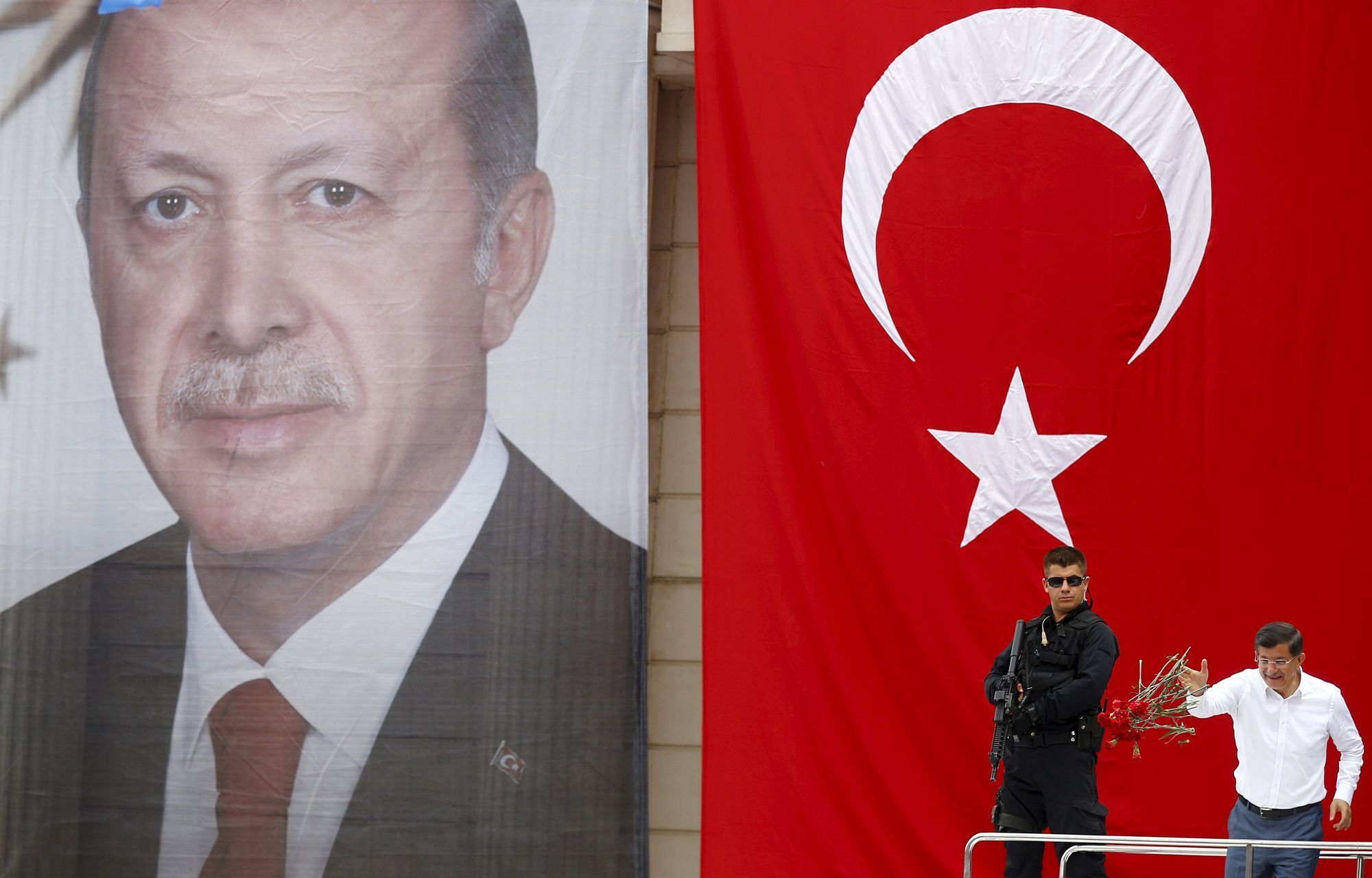 Turecký premiér Davutoglu (vpravo) na pódiu s obřím portrétem prezidenta Erdogana.