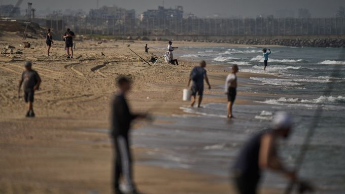 Na pozadí budov zničených během izraelských pozemních a vzdušných operací v severní části pásma Gazy se lidé snaží získat potravu rybařením.