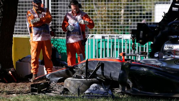 Course officials stand next to the car of McLaren Formula One driver Kevin Magnussen of Denmark after he crashed during the second practice session of the Australian F1 Grand Prix at the Albert Park c