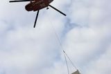 Pod vrtulníkem jsou v podvěsu přepravovány základnové stanice mobilní sítě třetí generace. Před dvěma lety operátor testoval jejich provoz v Nuslích, teď je potřebuje přesunout na střechy ve Vysočanech.