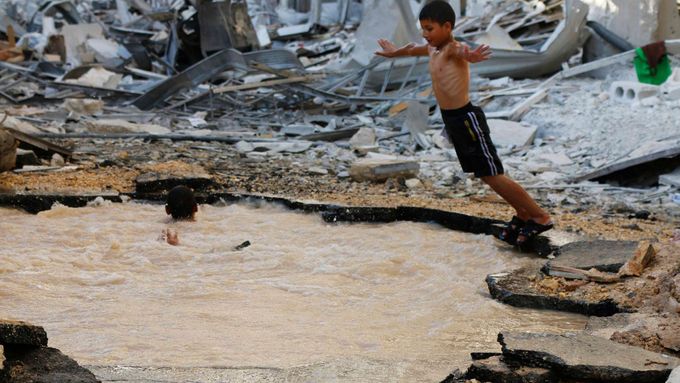 Ve vodě v kráteru po barelové bombě v syrském Aleppu se koupou děti. Později si ji možná přijdou načerpat místní.