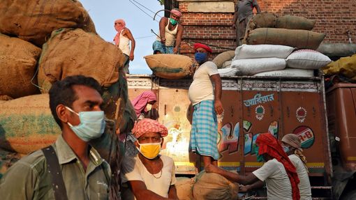 Pracovníci na indickém trhu vykládají pytle s potravinami během epidemie covidu-19.