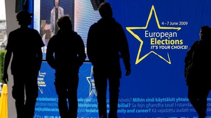 Momentka z Bruselu: Lidé kráčí kolem poutače, který láká k volbám do Evropského parlamentu. Plakát visí na Evropském parlamentu.
