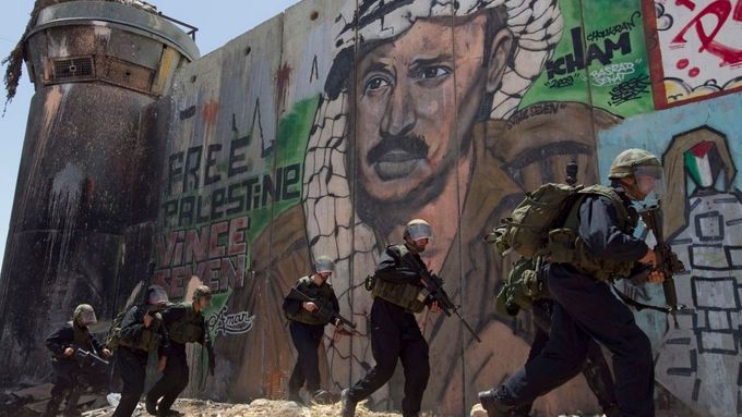 Zeď v Ramalláhu s portrétem Jásira Arafata, pod ní izraelští vojáci