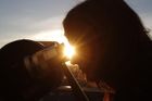 Záběr ze stejného místa. Žena vyhlíží skrze teleskop, kdy se v popředí před Sluncem objeví silueta Venuše.