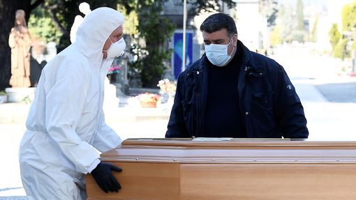 Muži v ochranných maskách přepravují rakev osoby, která zemřela na koronavirus. Život v Itálii během probíhající pandemie koronaviru Covid-19. Březen, 2020.