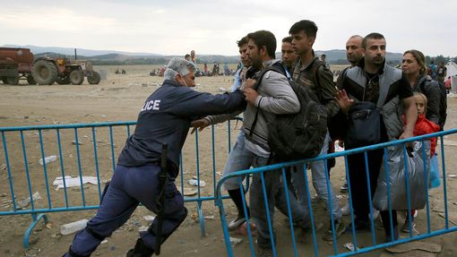 Řecký policista tlačí uprchlíky zpět za bariéru.