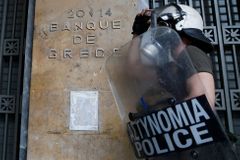 Policejní těžkooděnec střeží budovu centrální banky v Aténách.