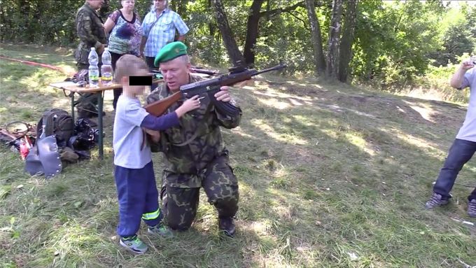 Branný den v Orlové. Muž s nášivkou Národní domobrany ukazuje dítěti zbraň.
