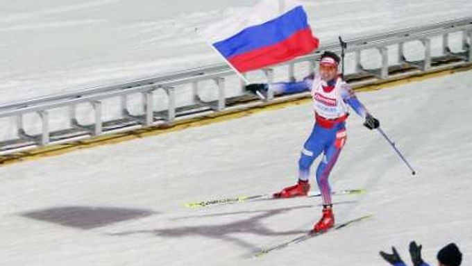 Nikolaj Kruglov vjíždí s ruskou vlajkou vítězně do cíle biatlonové štafety na 4x7,5 km.