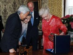 Královna Alžběta si prohlíží dárek, který včera dostala od japonského císařa Akihita. V pozadí její manžel princ Filip.