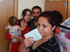 Muhammad se svojí rodinou. V popředí drží další syrská uprchlice kartu, kterou dostává každý, kdo požádá o azyl.