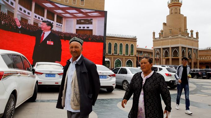 Ujgurové v Sin-ťiangu míjí obrazovku s čínským prezidentem Si Ťin-pchingem.