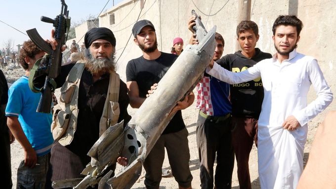 Islamisté a místní obyvatelé v syrském města Rakka s kusy vraku syrského vojenského letounu.