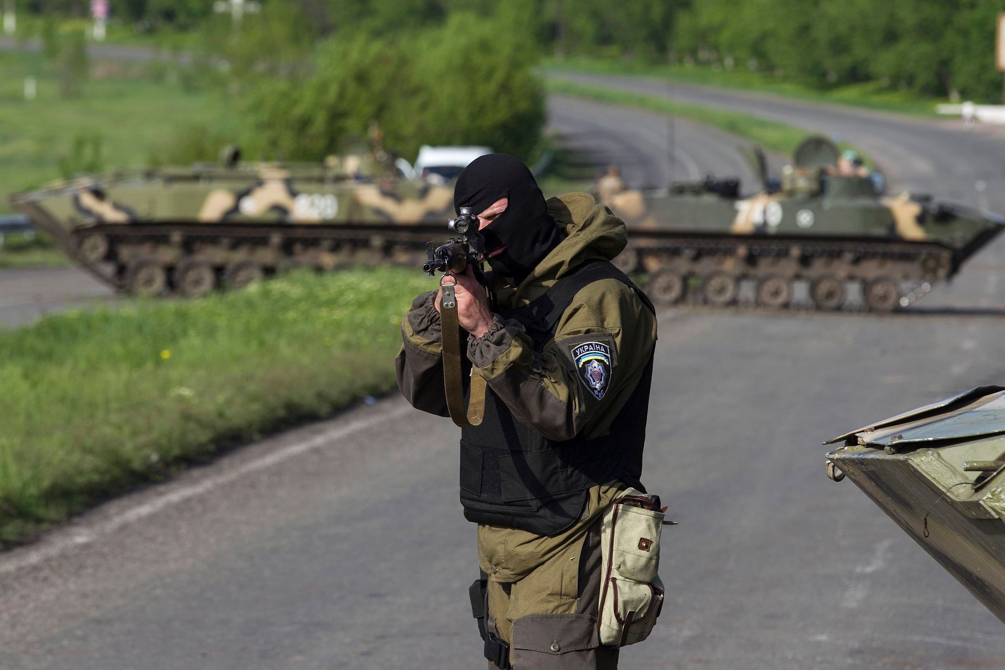 A Ukrainian soldier, with armoured personnel carriers behind him, points his weapon at an approaching car at a checkpoint near the town of Slaviansk in eastern Ukraine