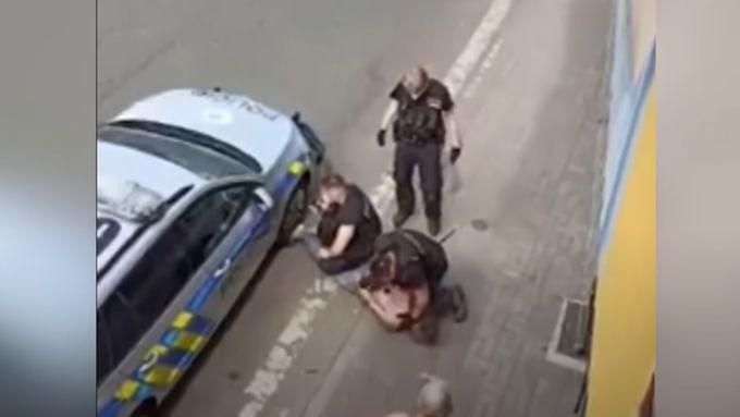 Záběr na policisty v Teplicích zdolávající Stanislava Tomáše, jeden mu klečí na krku.