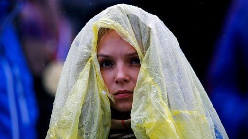 A spectator uses a raincover to protect herself from rain as she waits for the start of s