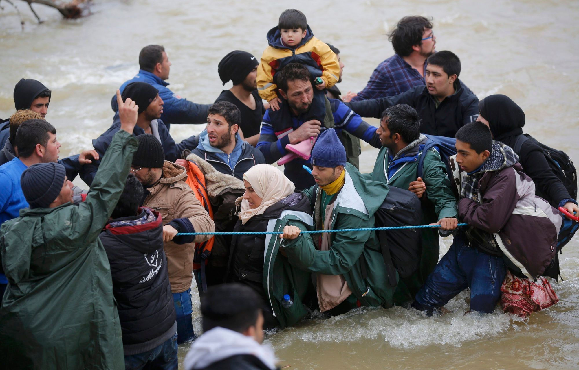 Běženci se brodí řekou, aby se dostali přes uzavřenou hranici mezi Řeckem a Makedonií.