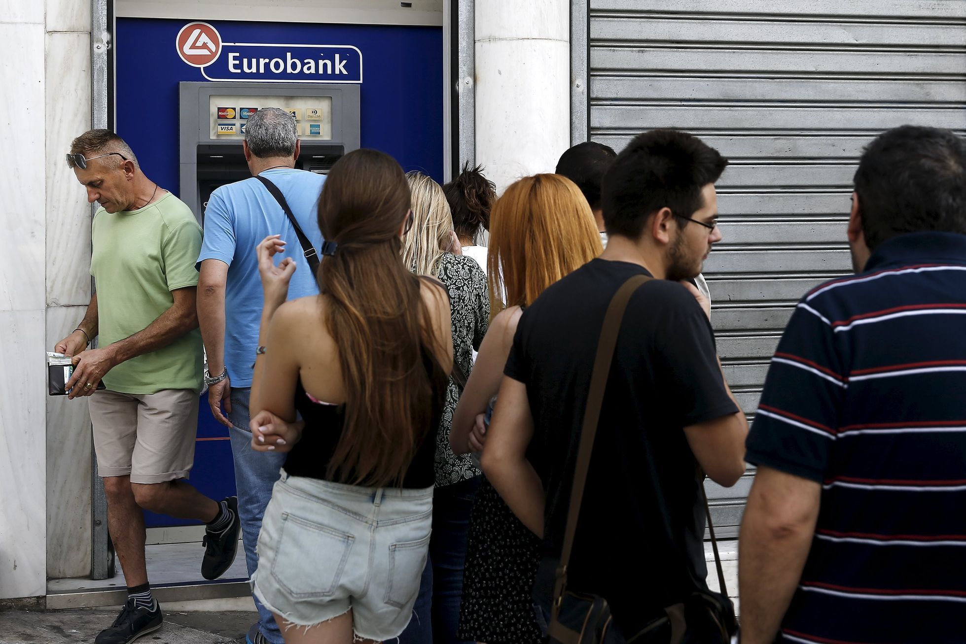 A man puts money in his wallet as people line up to withdraw cash from an ATM outside a Eurobank branch in Athens