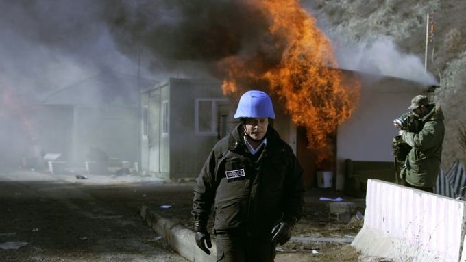 Příslušník mise UNMIK před hořící budovou v Jarinje.
