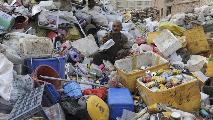 An elderly Uighur man sits on piles of garbage as he picks out the recyclable items at a recycling centre in Aksu